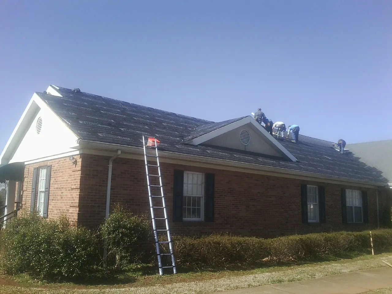 Crew tearing shingles off a brick ranch roof with a ladder set — Emergency Roof Repair work by our crew in Koosharem