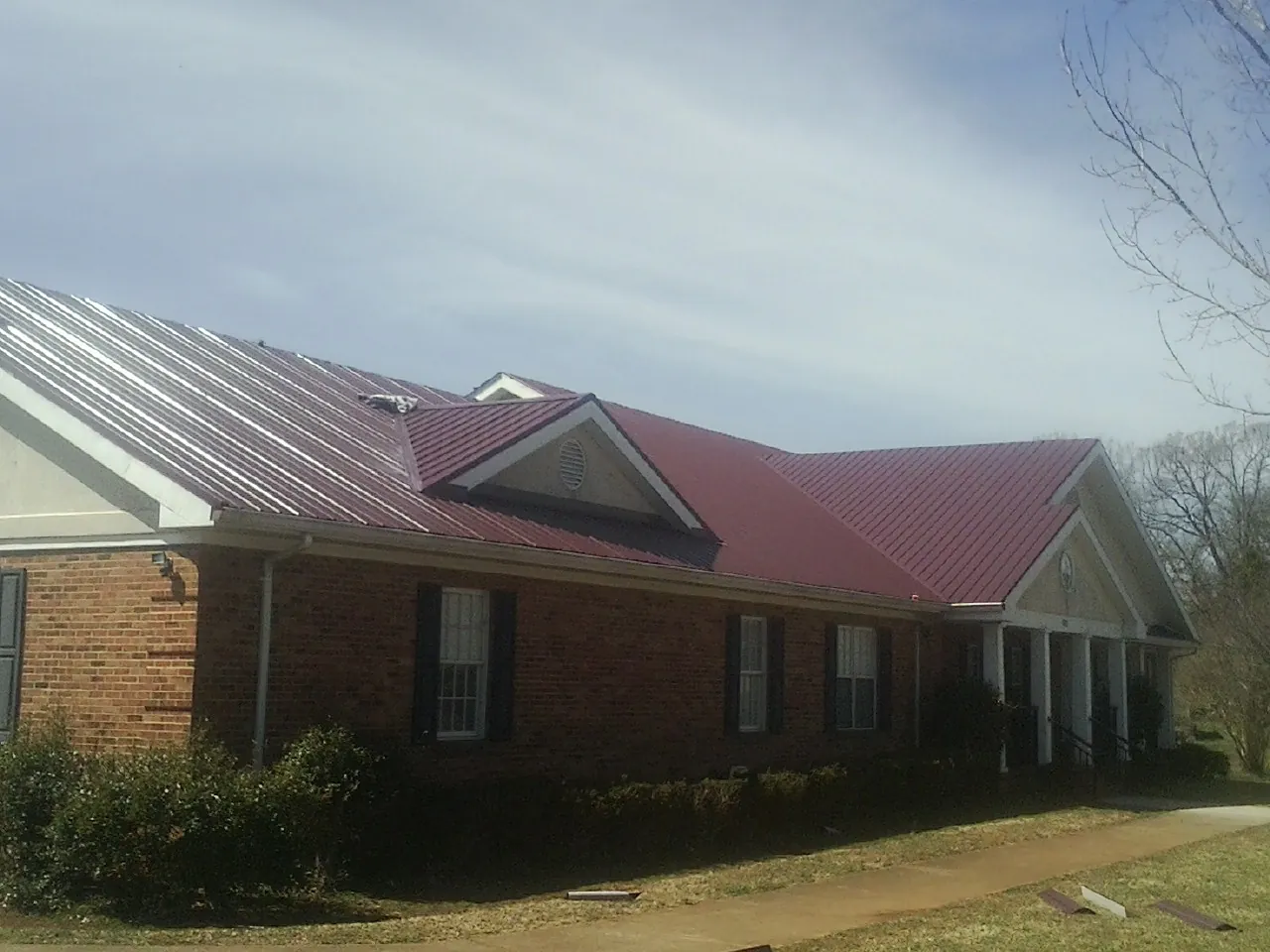 Red metal roof with gabled entries on a long brick building, from a Hail Damage Roof Repair job in Koosharem