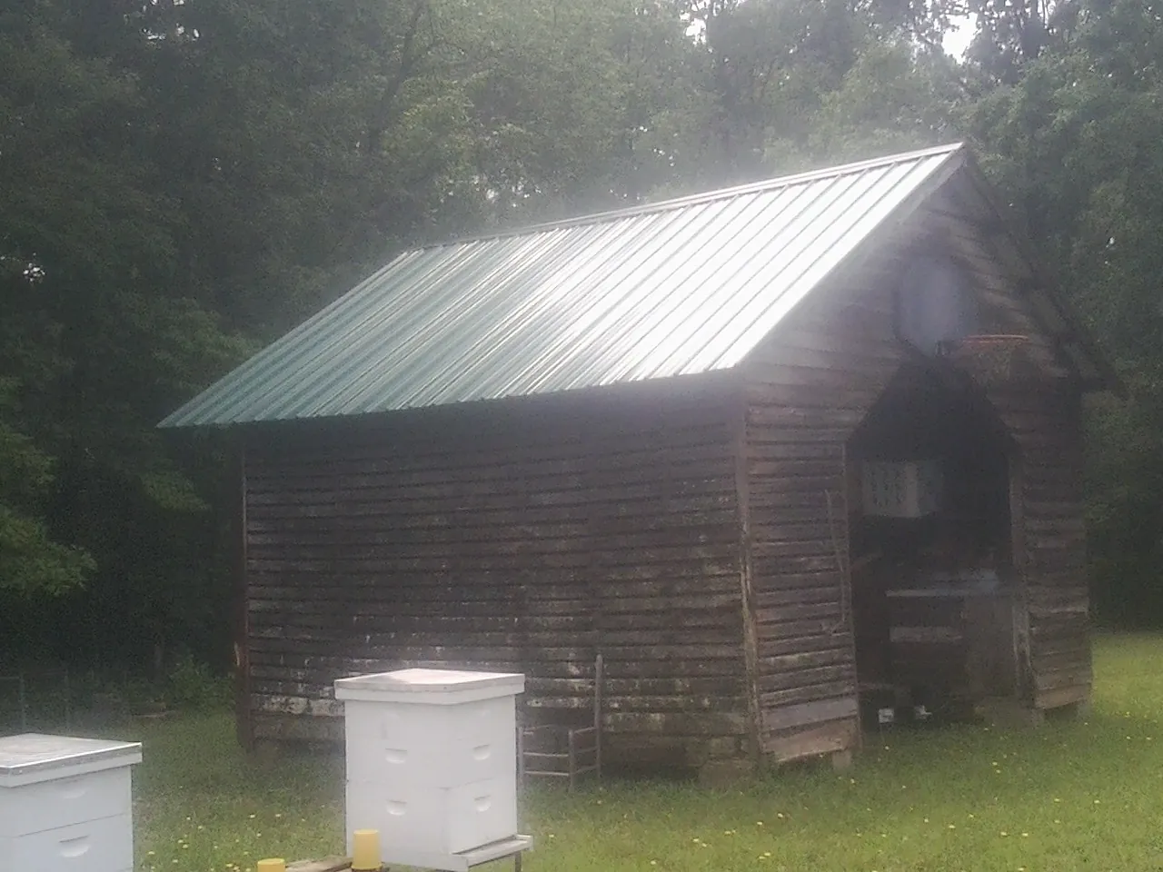 Green metal roof on a weathered barn beside stacked beehives in Koosharem