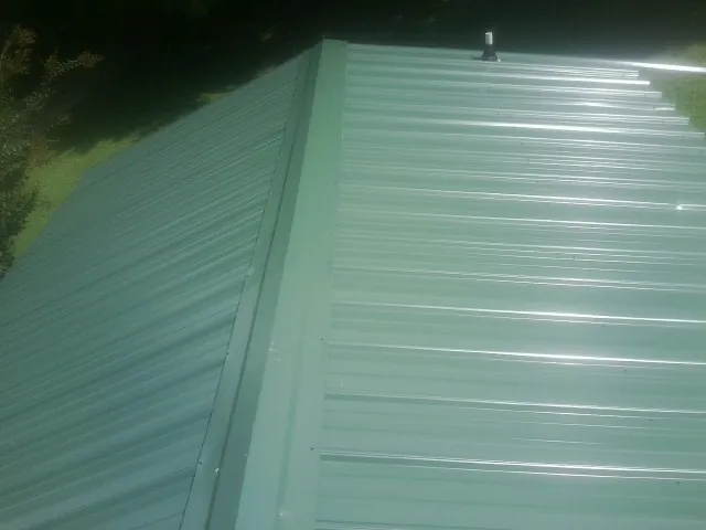 New green metal panels meeting at the ridge of a roof — Flat Roof Repair work by our crew in Koosharem