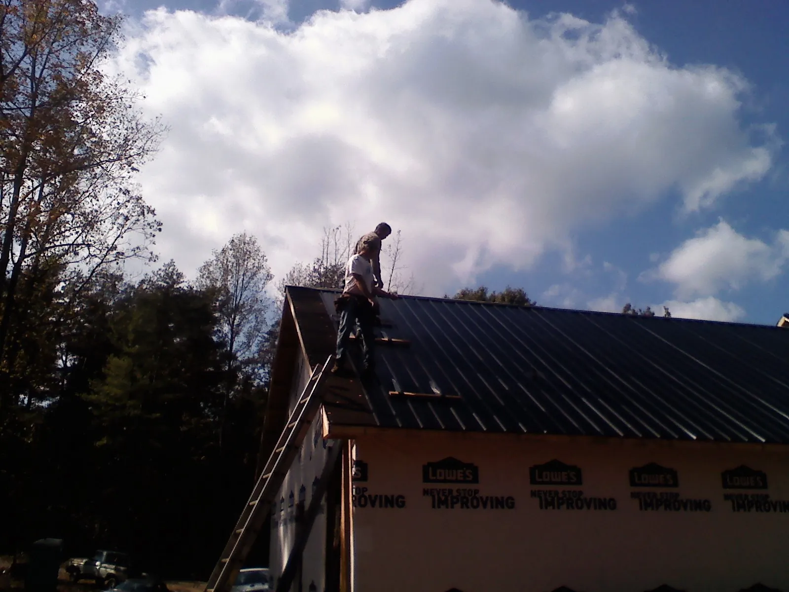 Roofer fastening dark metal panels high against a cloudy sky, from a Roof Inspection job in Koosharem